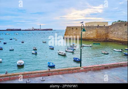 Le piccole barche, ormeggiate sulla riva di Cadice con i castelli medievali di San Sebastian e Santa Catalina, Cadice, Spagna Foto Stock