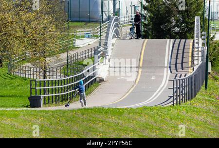 Il ciclista si è fermato alla pista ciclabile, c'è un bambino con uno scooter sotto. 24 aprile 2023, Bielorussia, Minsk Foto Stock