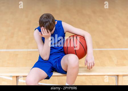 Triste ragazzo deluso con palla di basket in una lezione di educazione fisica Foto Stock