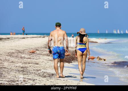 Coppia a piedi sulla sabbia sulle onde del mare e barche a vela sfondo. Spiaggia soleggiata con località turistica Foto Stock