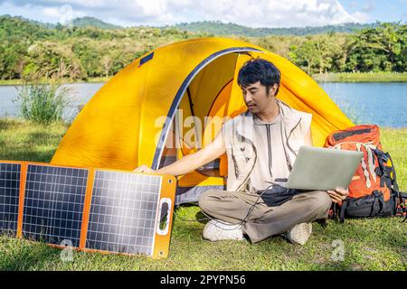 Giovane uomo di viaggio rilassarsi e godersi il campeggio . Spina maschio a mano in pannello solare portatile carica computer portatile con cavo multiuso Foto Stock