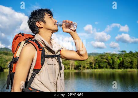 Giovane uomo asiatico zaino in spalla in viaggio nella foresta. Il viaggiatore di sesso maschile può contenere una bottiglia d'acqua. Sano escursionista bere acqua in escursione natura. Foto Stock