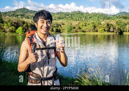 Bel giovane viaggiatore asiatico di sesso maschile riposante nella natura, tenendo una bottiglia d'acqua in natura. Risorsa naturale, giovane uomo che vive la vita attiva Foto Stock