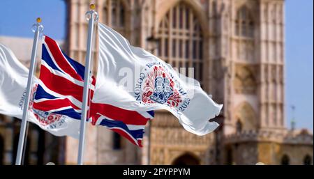 Londra, Regno Unito, aprile 2023: Bandiere con l'emblema dell'incoronazione di Re Carlo III e del Regno Unito che sventolano con Westminster Abbey sullo sfondo. Illustr Foto Stock