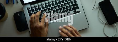 Lunghe ore di lavoro. Vista dall'alto dello spazio di lavoro di un giovane ragazzo che lavora su un computer portatile, seduto al tavolo in una stanza buia a tarda notte Foto Stock