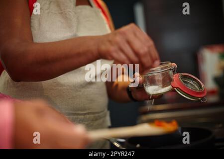 Condito con amore. Primo piano di due persone che cucinano un pasto insieme a casa. Foto Stock