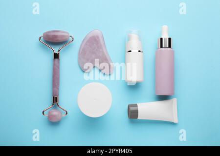 Composizione piatta con strumento gua sha e, rullo facciale e prodotti per la cura della pelle su sfondo azzurro Foto Stock