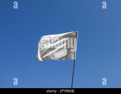 Bandiera bianca che sbatte contro il cielo blu nelle giornate di sole Foto Stock