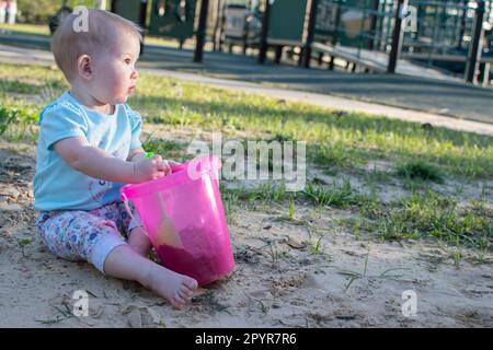 Bambino caucasico giocare con la sabbia vicino al parco giochi in una giornata di sole Foto Stock