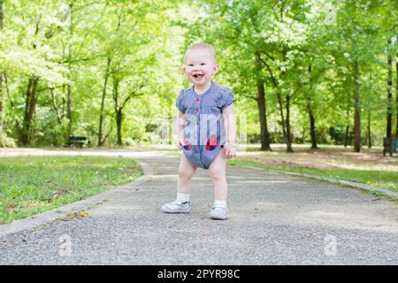 Un bambino sta facendo i suoi primi passi nel parco. Il bambino sta imparando come camminare. Sviluppo del bambino 1-year-old ragazza Foto Stock