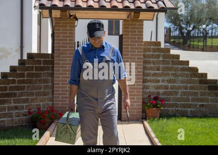 Immagine di un manipolo in tute e cassetta degli attrezzi sulla strada per una casa dopo una chiamata. Lavori di riparazione fai da te di un idraulico ed elettricista Foto Stock