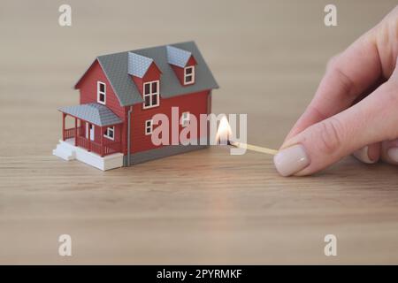 Mano di donna che tiene partita per bruciare casa su tavolo di legno Foto Stock