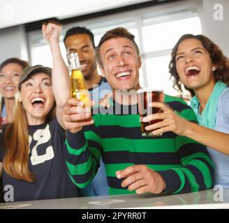 Alzando i loro occhiali ad un gioco impressionante. Un gruppo di amici che allietano la loro squadra preferita al bar. Foto Stock