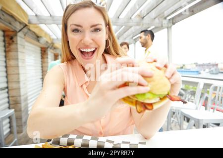 Im prendere questo hamburger giù. Ritratto di una bella giovane donna che mangia un hamburger enorme e delizioso in un ristorante. Foto Stock