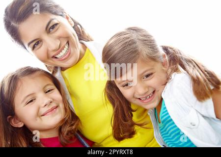 Due ragazze e la loro madre. Portrait di una giovane madre che abbraccia le sue figlie affettuosamente su uno sfondo luminoso. Foto Stock