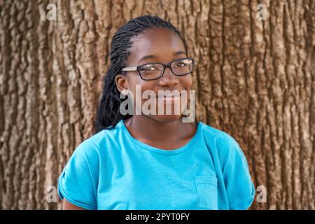 Non cisce un hugger dell'albero ma lei lo ama sicuro. Ritratto di una bella teen nera sorridente mentre in piedi contro un albero. Foto Stock