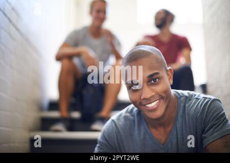 HES che lo farà in questo college. Ritratto di uno studente universitario maschio seduto con i suoi amici sui gradini di una scala. Foto Stock