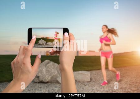 Immagine ravvicinata delle mani femminili che tengono il telefono cellulare con la modalità fotocamera sullo schermo. Immagine ritagliata di una donna in corsa. Runner jogging al sole Foto Stock