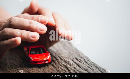 Le mani femminili e l'automobile come protezione del concetto dell'automobile. Donna agente di assicurazione che copre l'auto giocattolo su sfondo bianco, primo piano. Protezione delle mani dell'auto Foto Stock