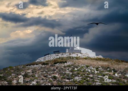 Piccola cappella greca bianca in piedi su una collina sotto un cielo drammatico Foto Stock