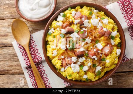 Corn porridge servito con formaggio, cipolla fritta e pancetta closeup sulla ciotola sul tavolo di legno. Vista orizzontale dall'alto Foto Stock
