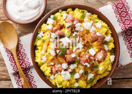 Gustoso banosh servito con brynza, cipolla fritta e cracklings di maiale su tavolo di legno, primo piano. Vista orizzontale dall'alto Foto Stock