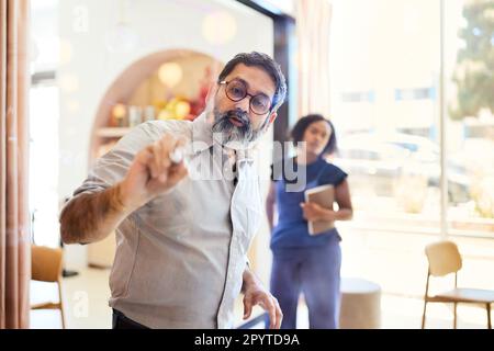 Uomo maturo imprenditore scrittura su parete di vetro con collega femmina Foto Stock