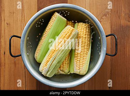 Pronto per il piano cottura. Colpo ad angolo alto di pannocchie di mais in un colino su un tavolo. Foto Stock