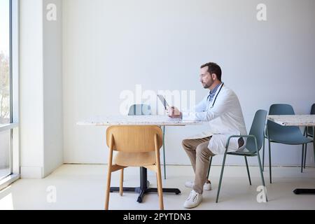 Vista laterale di un medico maschio che usa un tablet PC mentre si siede sulla sedia Foto Stock