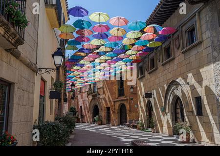 Ombrelloni sospesi e Uniti tra loro in una strada di Poble Espanyol per formare un tetto di ombrelloni colorati, Barcellona, Spagna. Foto Stock