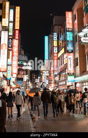 TOKYO, GIAPPONE - 8 APRILE 2023: Persone che camminano nella zona commerciale di Shibuya in serata piovente Foto Stock