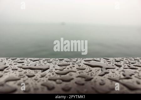 nuvoloso, piovoso, giorno d'autunno sulla riva di un grande lago, nebbia sull'acqua sotto forma di una foschia grigia, gocce d'acqua prese in primo piano Foto Stock