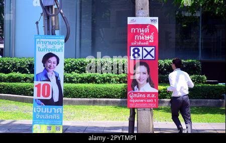 I candidati alle elezioni utilizzano i cartelli appesi ai mobili per la strada per pubblicizzare se stessi ai potenziali elettori del distretto di Silom, nel centro di Bangkok, in Thailandia. Le elezioni generali si terranno in Thailandia il 14th maggio 2023, dopo lo scioglimento della 25th Camera dei rappresentanti il 20th marzo 2023. Un uomo passa davanti a un cartello elettorale o campagna. Foto Stock