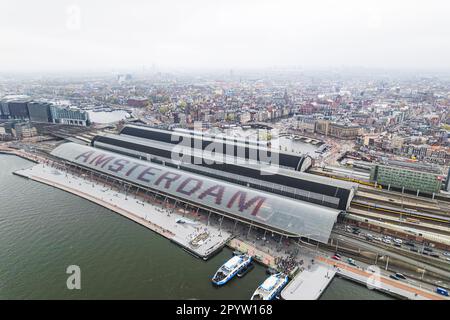 Vista aerea della stazione ferroviaria centrale di NS. Il nome di Amsterdam è scritto come simbolo enorme sul tetto. I traghetti per attraversare il fiume IJ sono nel porto. Foto di alta qualità Foto Stock