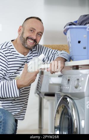uomo allegro che mette i vestiti sporchi sulla lavatrice Foto Stock