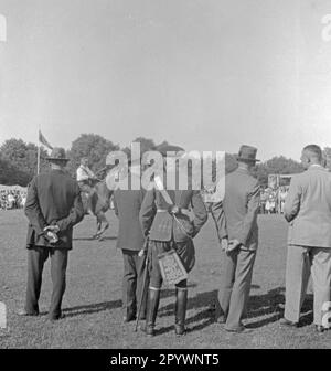 Gli spettatori guardano il ring a Warnemünde. Nella corsa ad anello, una lancia è messa attraverso un anello appeso ad un ponteggio. L'uomo al centro indossa un'uniforme dell'esercito prussiano. Foto Stock