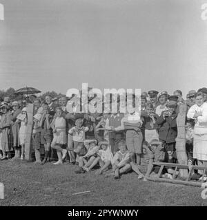 Un gruppo di spettatori guarda l'anello suonare a Warnemünde. Nella corsa ad anello, una lancia è messa attraverso un anello appeso ad un ponteggio. Foto Stock