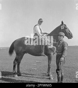 Un cavaliere e il suo cavallo partecipano al ring riding a Warnemünde. Davanti al cavallo c'è un uomo SA, che probabilmente assegna un premio. Foto Stock