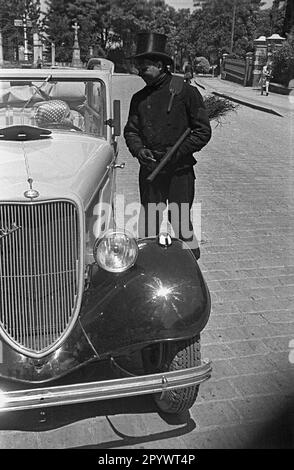 Una donna al volante di un'auto che parla con un camino spazzare. A Wuenschelburg (oggi Radkow) nella bassa Slesia. Foto Stock