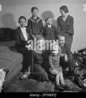 Una famiglia si sta preparando per una foto comune. L'albero di Natale e i vestiti di festa suggeriscono che questa è una foto tradizionale di Natale. Foto Stock