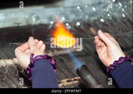 Il soffiatore di vetro riscalda il pezzo di vetro per dare forma al futuro ornamento natalizio Foto Stock