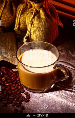 Tazza di caffè in vetro con sacchi di caffè crudo tostato Foto Stock