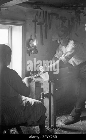 Un uomo di Silesian Albendorf lavora su un pezzo di legno insieme ad una donna. La stringa indica che si tratta di un tornio. Ci sono diversi strumenti appesi alla parete. Foto Stock