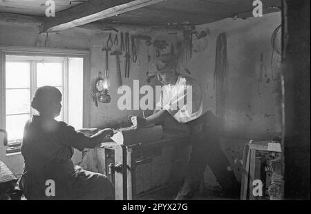 Un uomo nel villaggio silesiano di Albendorf trasforma un pezzo di legno con una donna. Ci sono diversi strumenti appesi alla parete. Foto Stock