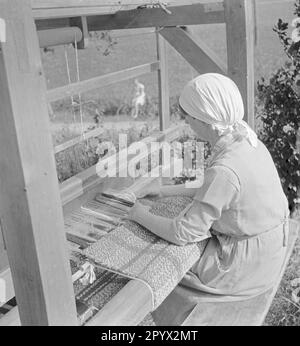 Una donna lavora su un telaio di fronte al mulino di tessitura. Foto Stock