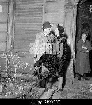 Un uomo e una donna flirt e dire addio a una porta. Sullo sfondo, una donna anziana. Foto Stock