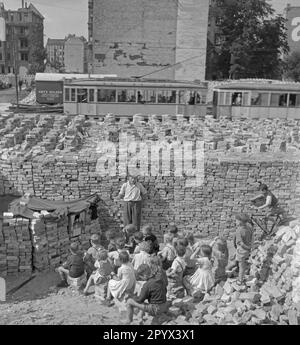 Foto non datata di un gruppo di bambini che guarda uno spettacolo di marionette tra mucchi di mattoni rimanenti dalle rovine. I mattoni servono come tenda del teatro delle marionette. Sullo sfondo, più pile di mattoni, un auto di passaggio e case parzialmente distrutte da bombardamenti. Foto Stock