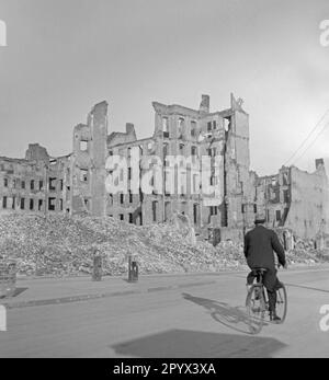 Foto non datata di un ciclista su una strada di fronte alla casa tramorerie a Berlino, presumibilmente Berlino Ovest, 1950. Le case distrutte dai bombardamenti sono parzialmente crollate. Ci sono mucchi di macerie accanto al marciapiede. Foto Stock