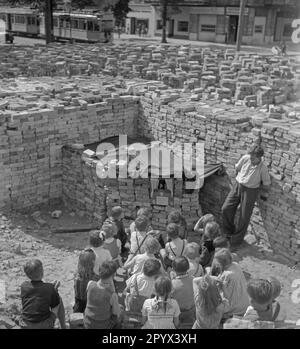 Foto non datata di un gruppo di bambini che guarda uno spettacolo di marionette tra mucchi di mattoni rimanenti dalle rovine. I mattoni servono come tenda del teatro delle marionette. A destra del palco, il burattinaio. Sullo sfondo, più pile di mattoni e un tram di passaggio. Foto Stock