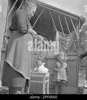 Foto di una anziana donna contadina in grembiule mentre equipaggiano una lampada a cherosene con un nuovo stoppino di fronte ad un fienile a Gut Osdorf a sud di Berlino nell'estate del 1936. È guardata da un bambino piccolo. Foto Stock